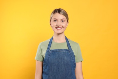 Beautiful young woman in denim apron on orange background