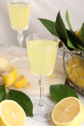 Tasty limoncello liqueur, lemons and green leaves on table
