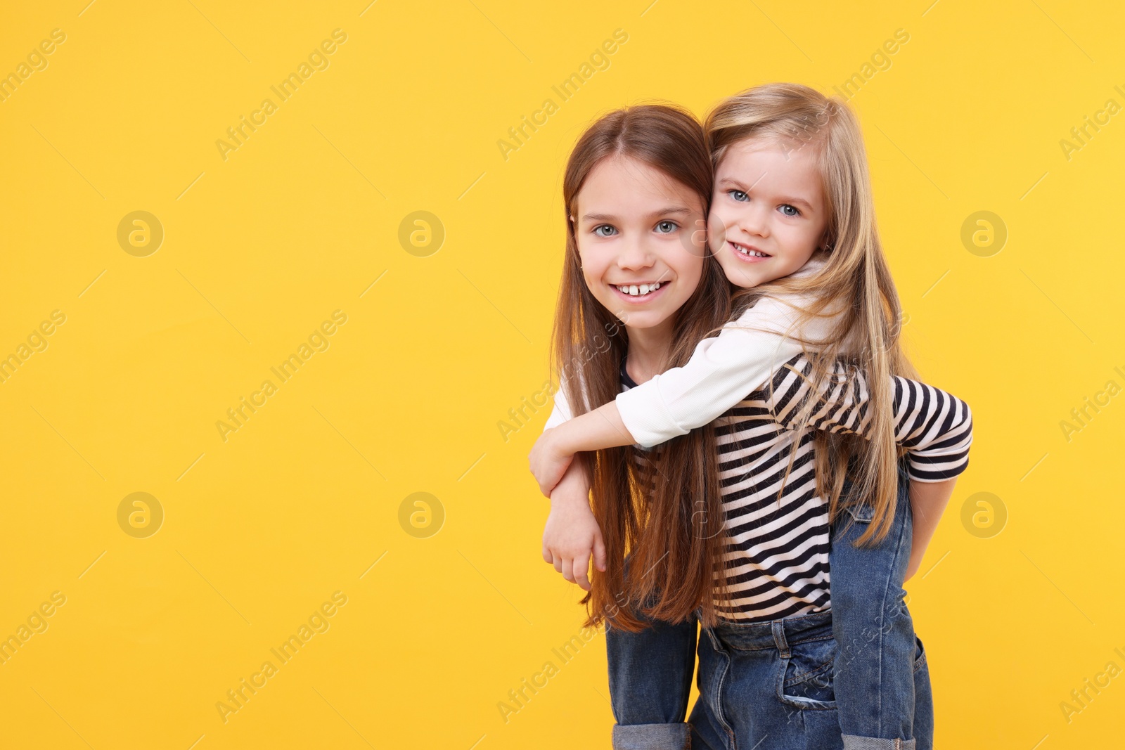 Photo of Portrait of cute little sisters on orange background, space for text