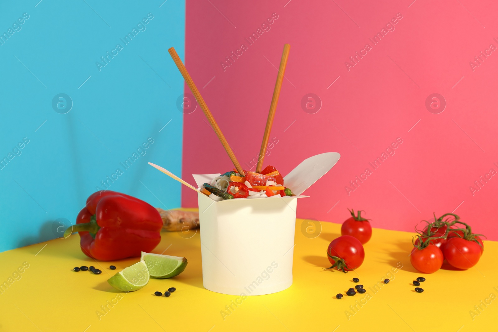 Photo of Box of vegetarian wok noodles with ingredients and chopsticks on color background