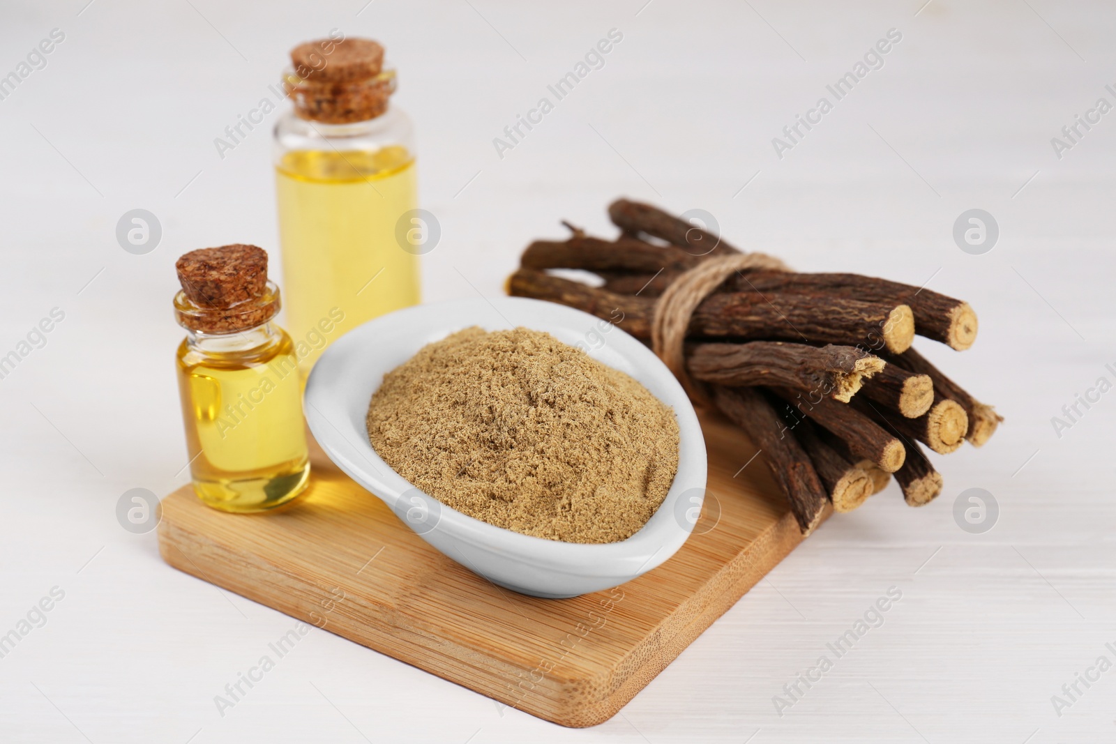 Photo of Dried sticks of licorice roots, bottles with essential oil and powder on white wooden table