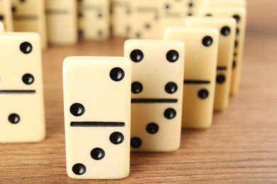 Photo of White domino tiles with black pips on wooden table, closeup