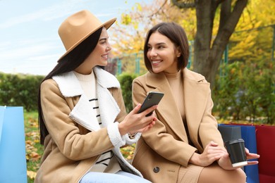 Special Promotion. Happy young women with smartphone and shopping bags in park