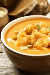 Photo of Tasty creamy pumpkin soup with croutons and seeds in bowl on wooden table, closeup