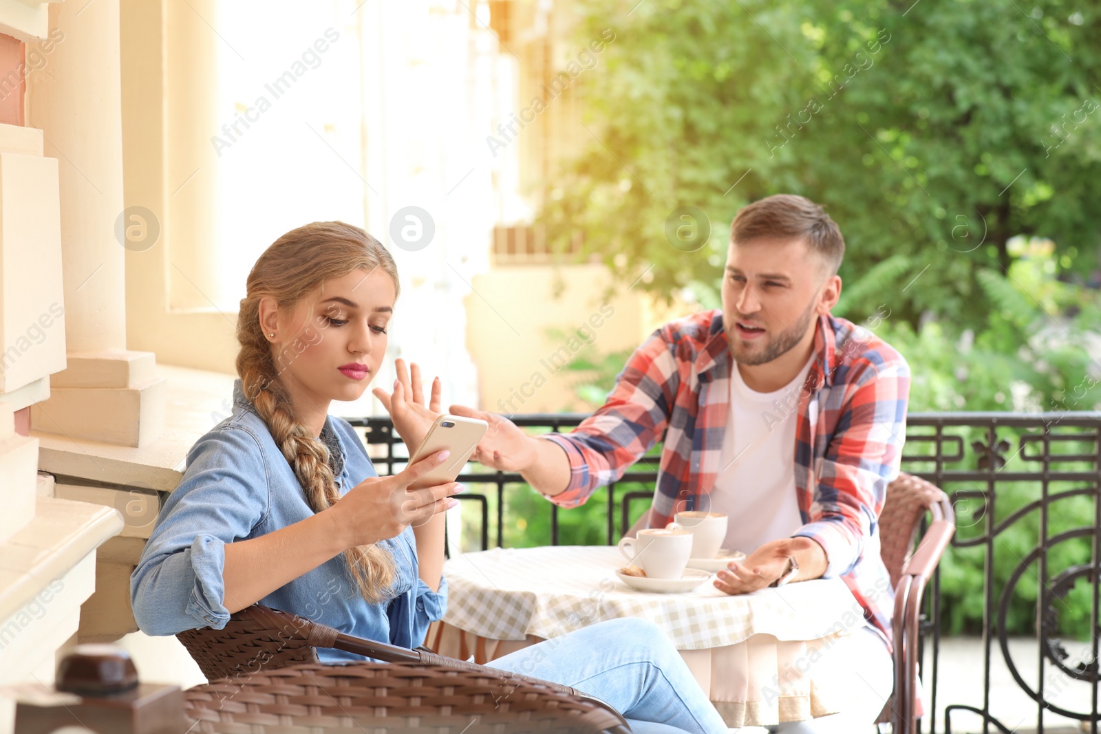 Photo of Young couple arguing while sitting in cafe, outdoors. Problems in relationship