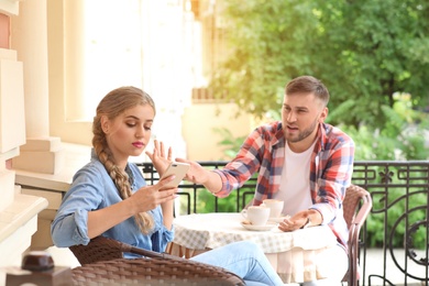 Photo of Young couple arguing while sitting in cafe, outdoors. Problems in relationship