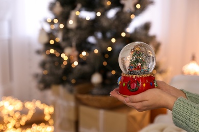 Photo of Woman holding snow globe near Christmas tree at home, closeup. Space for text