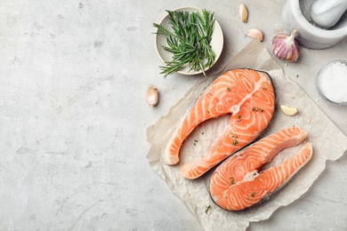 Photo of Fresh raw salmon steaks with seasonings on gray background, top view