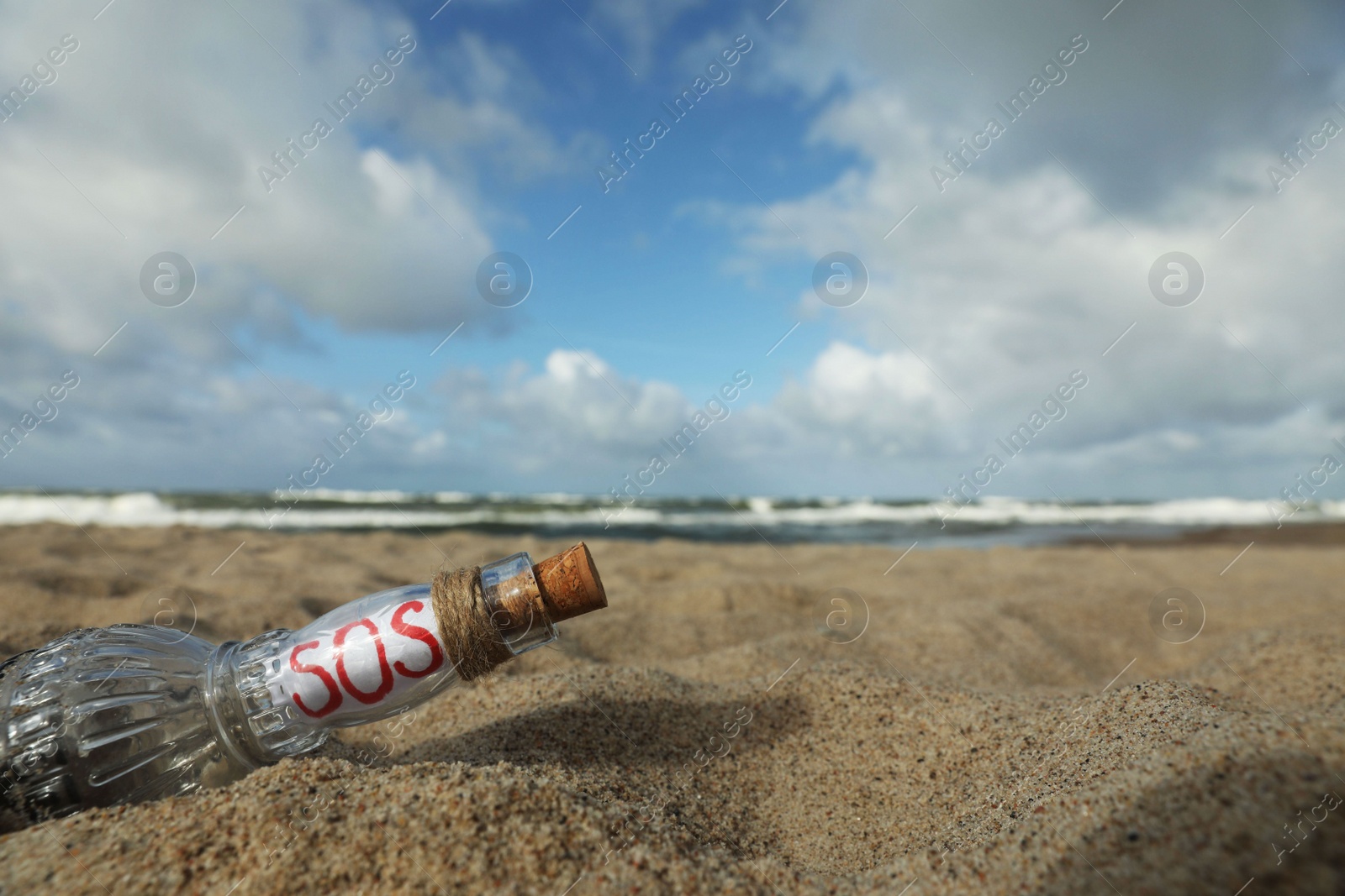 Photo of Glass bottle with SOS message on sand near sea, space for text