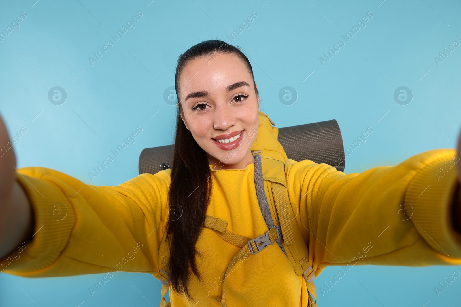 Photo of Smiling young woman with backpack taking selfie on light blue background. Active tourism