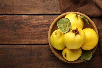 Photo of Tasty ripe quince fruits in bowl on wooden table, top view. Space for text