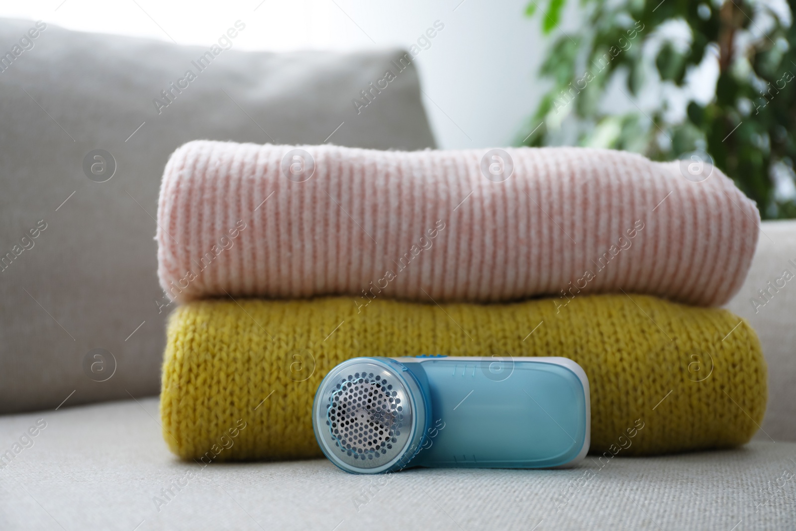 Photo of Modern fabric shaver and woolen sweaters on sofa indoors