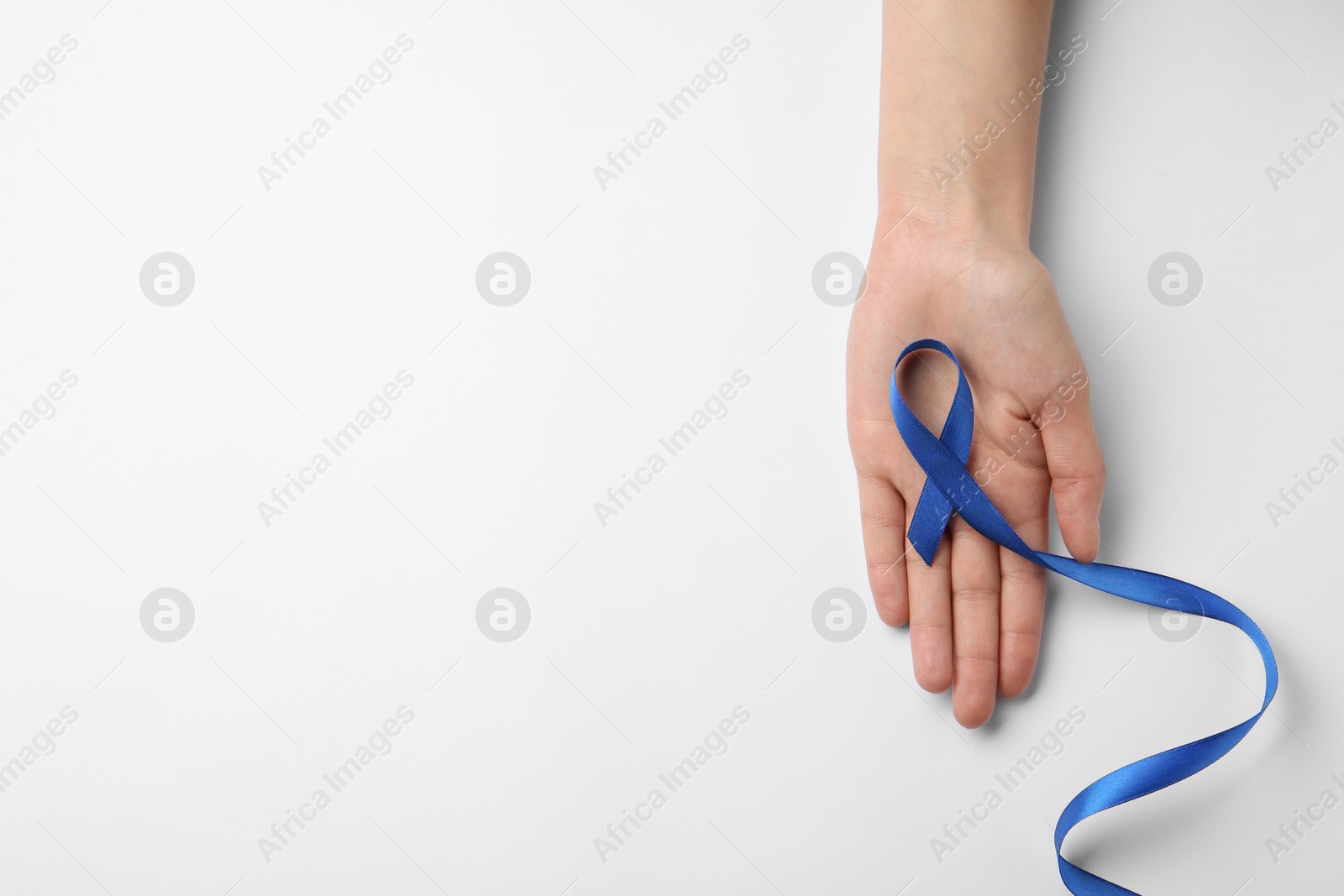 Photo of Woman holding blue awareness ribbon on white background, top view. Symbol of social and medical issues