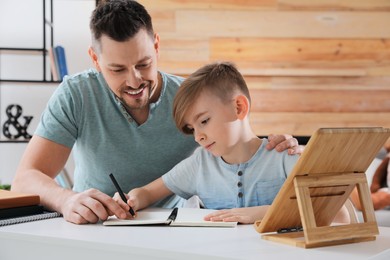 Photo of Boy with father doing homework at table indoors