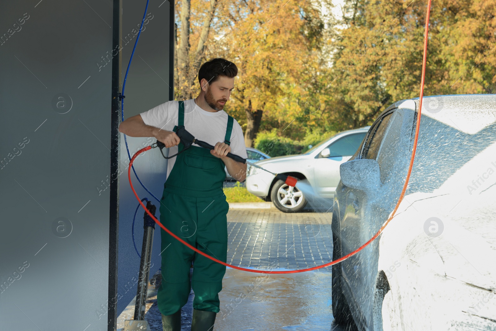 Photo of Worker washing auto with high pressure water jet at outdoor car wash