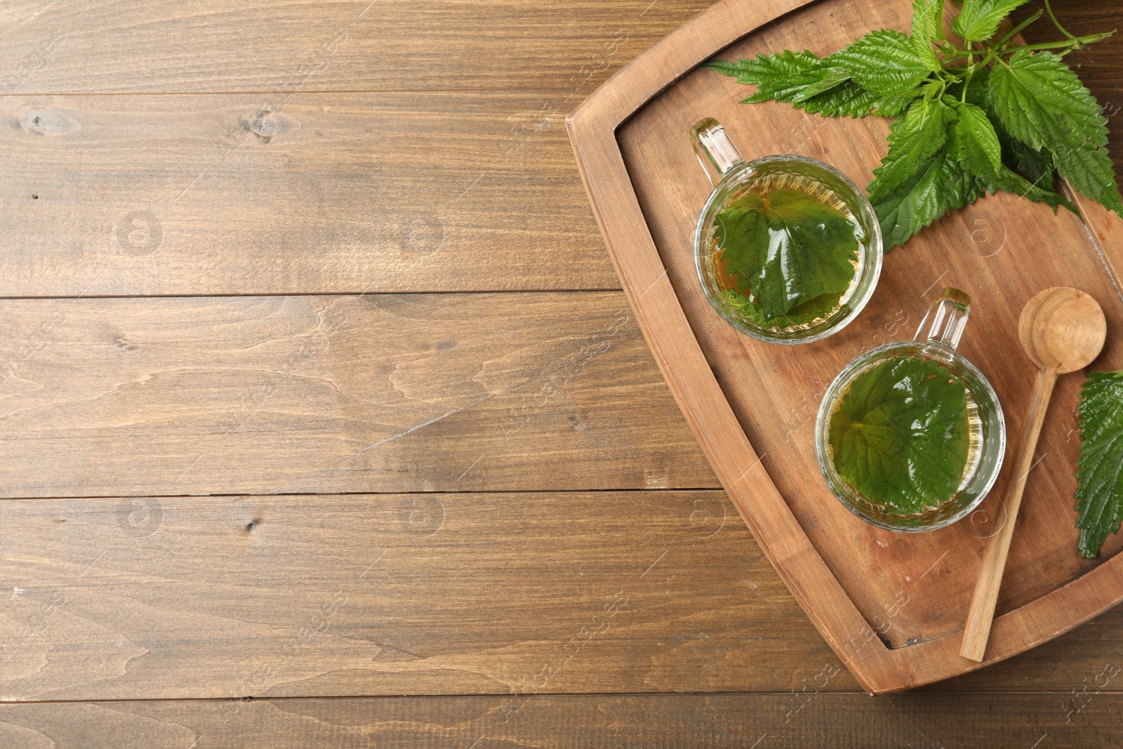 Photo of Glass cups of aromatic nettle tea and green leaves on wooden table, top view. Space for text