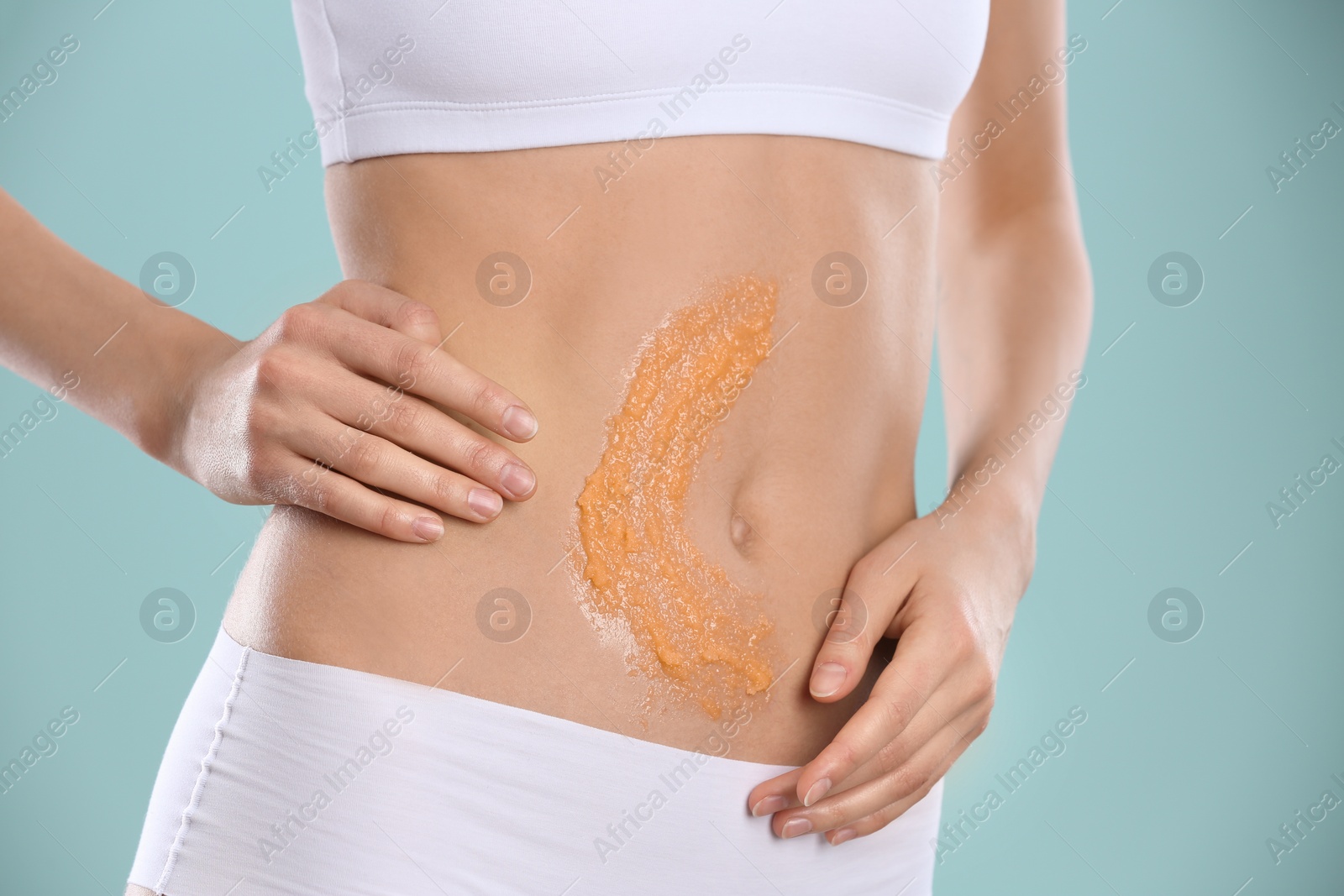 Photo of Young woman applying natural scrub on her belly against color background, closeup