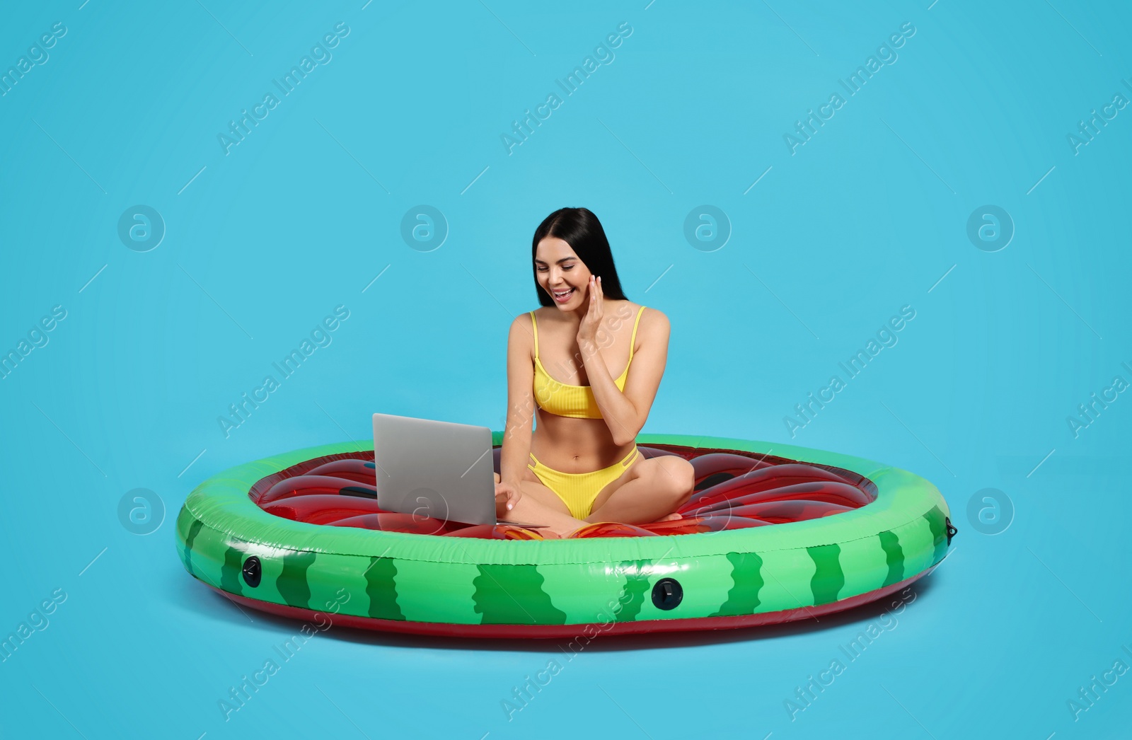 Photo of Young woman using laptop while sitting on inflatable mattress against light blue background
