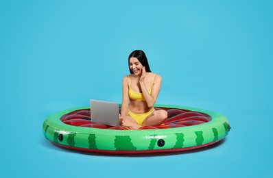 Young woman using laptop while sitting on inflatable mattress against light blue background