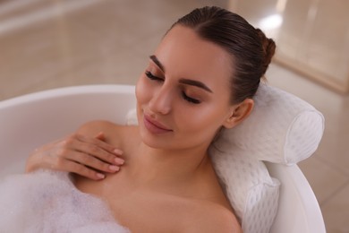 Photo of Young woman using pillow while enjoying bubble bath indoors