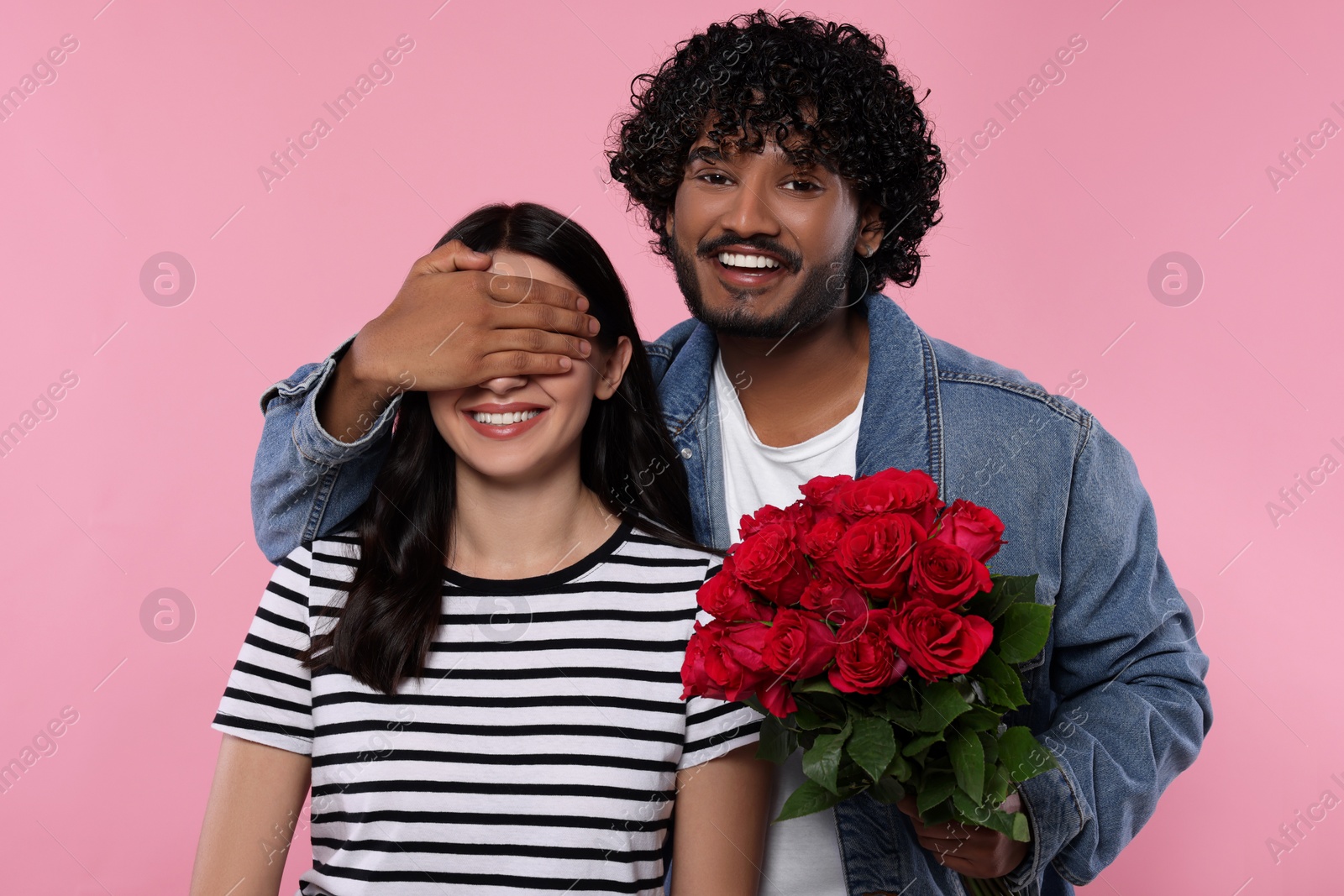 Photo of International dating. Handsome man presenting roses to his beloved woman on pink background