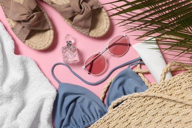 Flat lay composition with wicker bag and other beach accessories on pink background