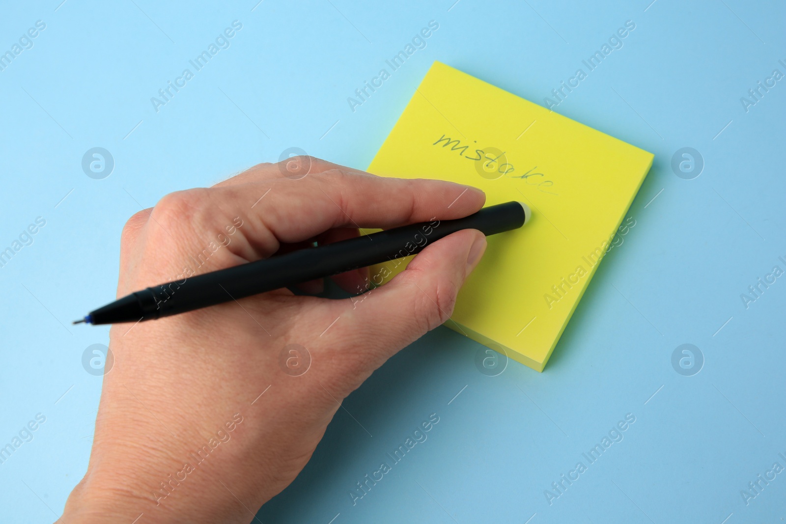 Photo of Woman erasing word Mistake written with erasable pen on paper notes against light blue background, closeup