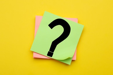 Photo of Sticky note with question mark on yellow background, top view