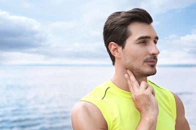 Young man checking pulse  after training on beach. Space for text