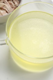 Photo of Glass pot with tasty bouillon on white marble table, above view