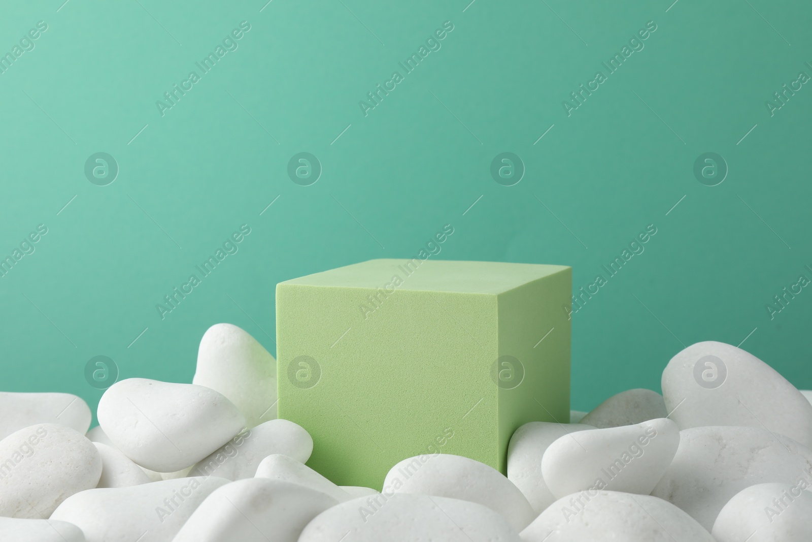 Photo of Presentation for product. Light green cube podium and white pebbles on color background. Space for text