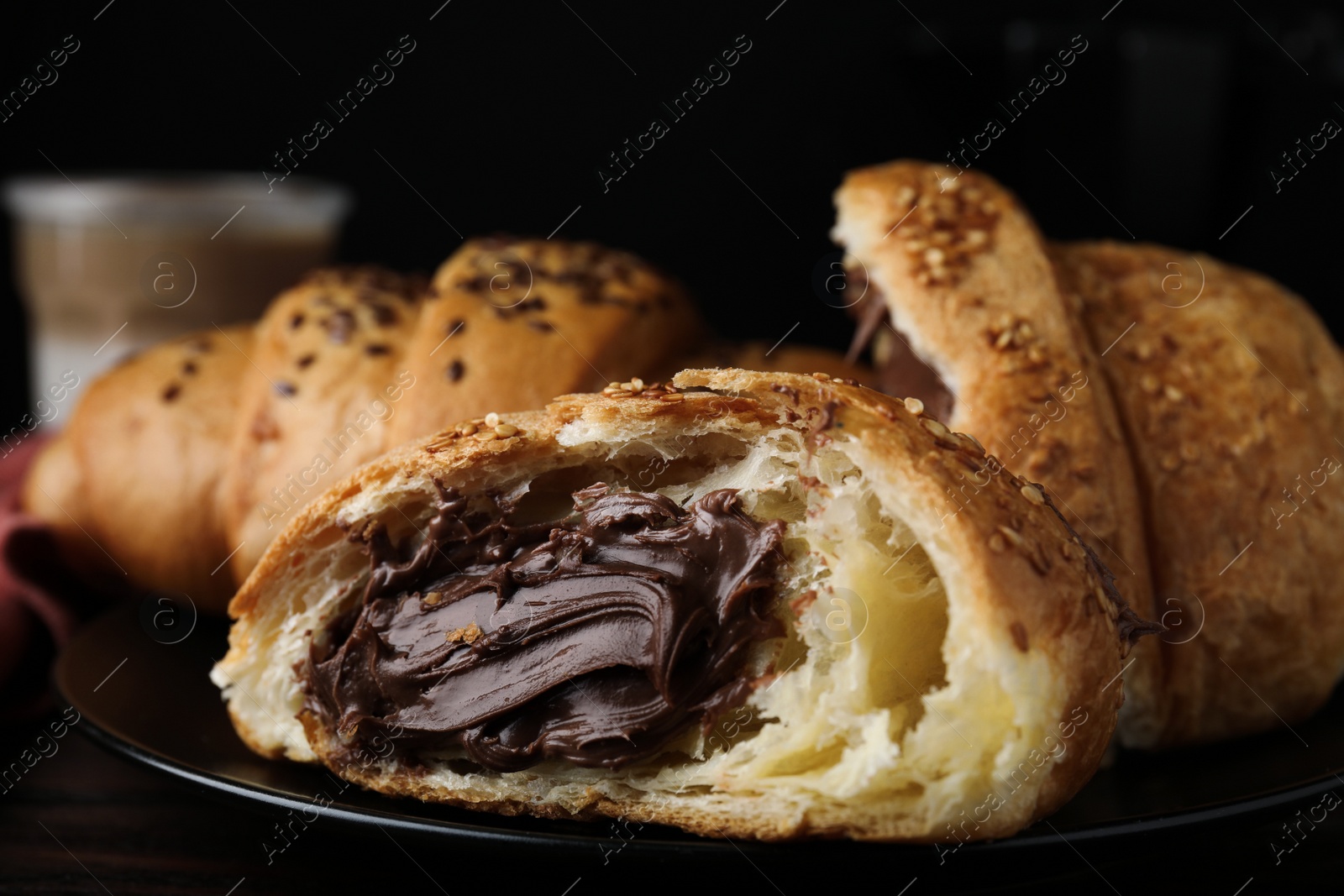 Photo of Tasty croissants with chocolate and sesame seeds on black plate, closeup