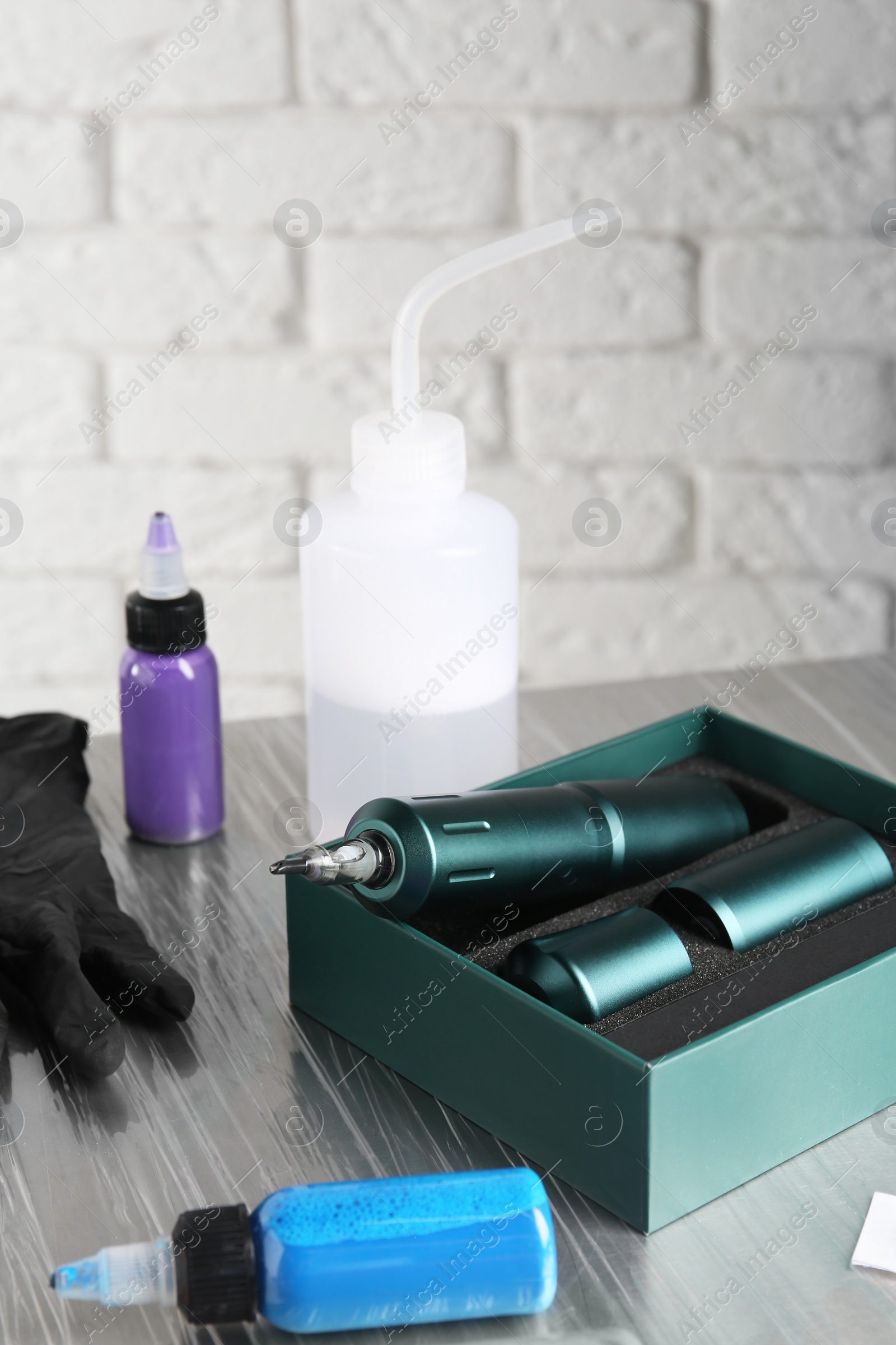 Photo of Modern professional tattoo machine and colorful inks on table in salon