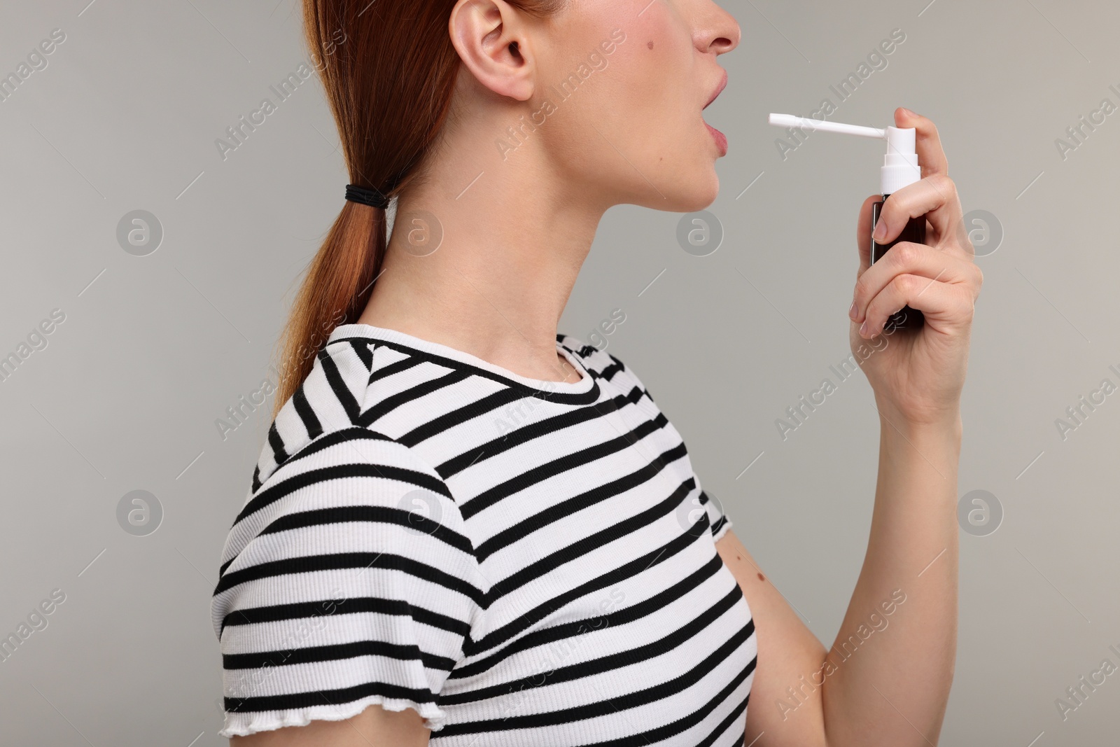 Photo of Young woman using throat spray on grey background, closeup