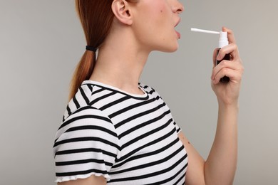 Photo of Young woman using throat spray on grey background, closeup