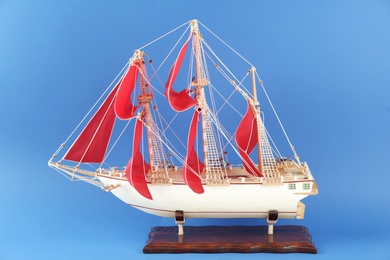 Photo of Miniature model of old ship with red sails on blue background