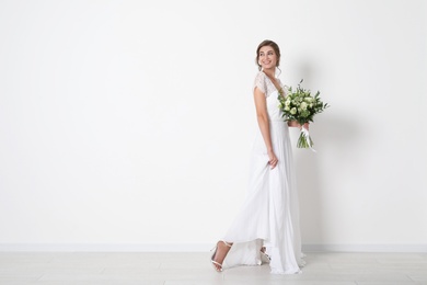 Photo of Young bride wearing wedding dress with beautiful bouquet near light wall. Space for text