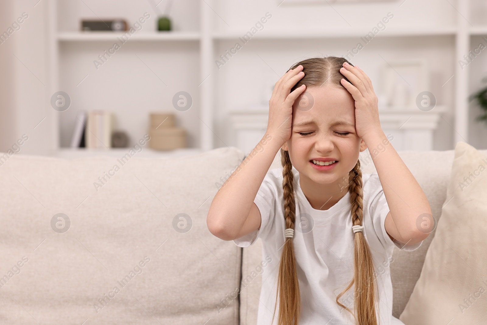 Photo of Little girl suffering from headache at home. Space for text