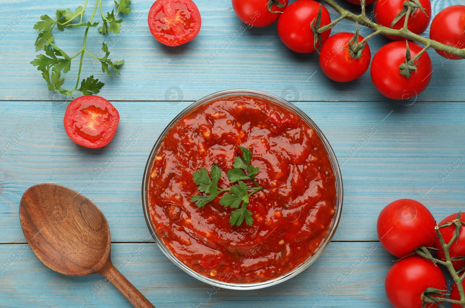 Photo of Delicious adjika sauce in bowl and ingredients on light blue wooden table, flat lay