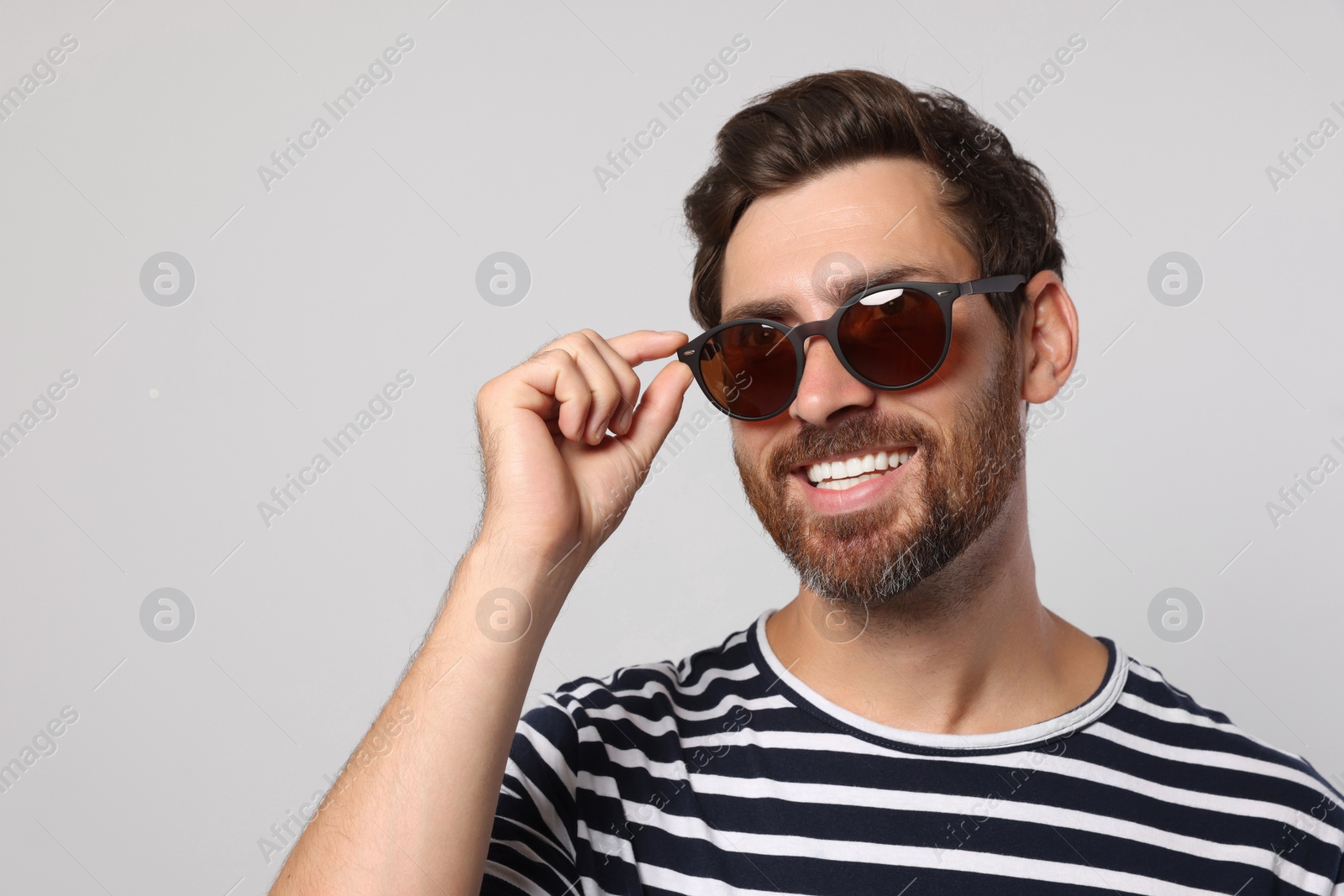 Photo of Portrait of smiling bearded man with stylish sunglasses on light grey background. Space for text
