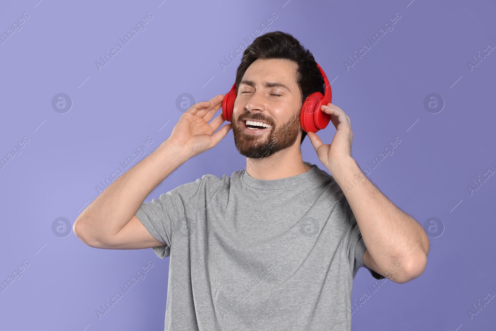Photo of Happy man listening music with headphones on violet background