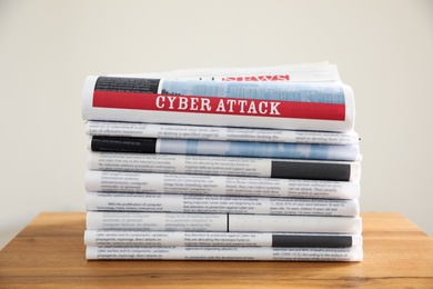 Newspapers with headline CYBER ATTACK stacked on wooden table indoors