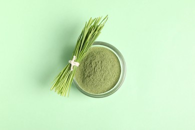Photo of Wheat grass powder in bowl and fresh sprouts on green table, top view
