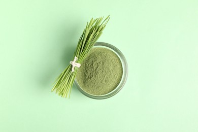 Wheat grass powder in bowl and fresh sprouts on green table, top view