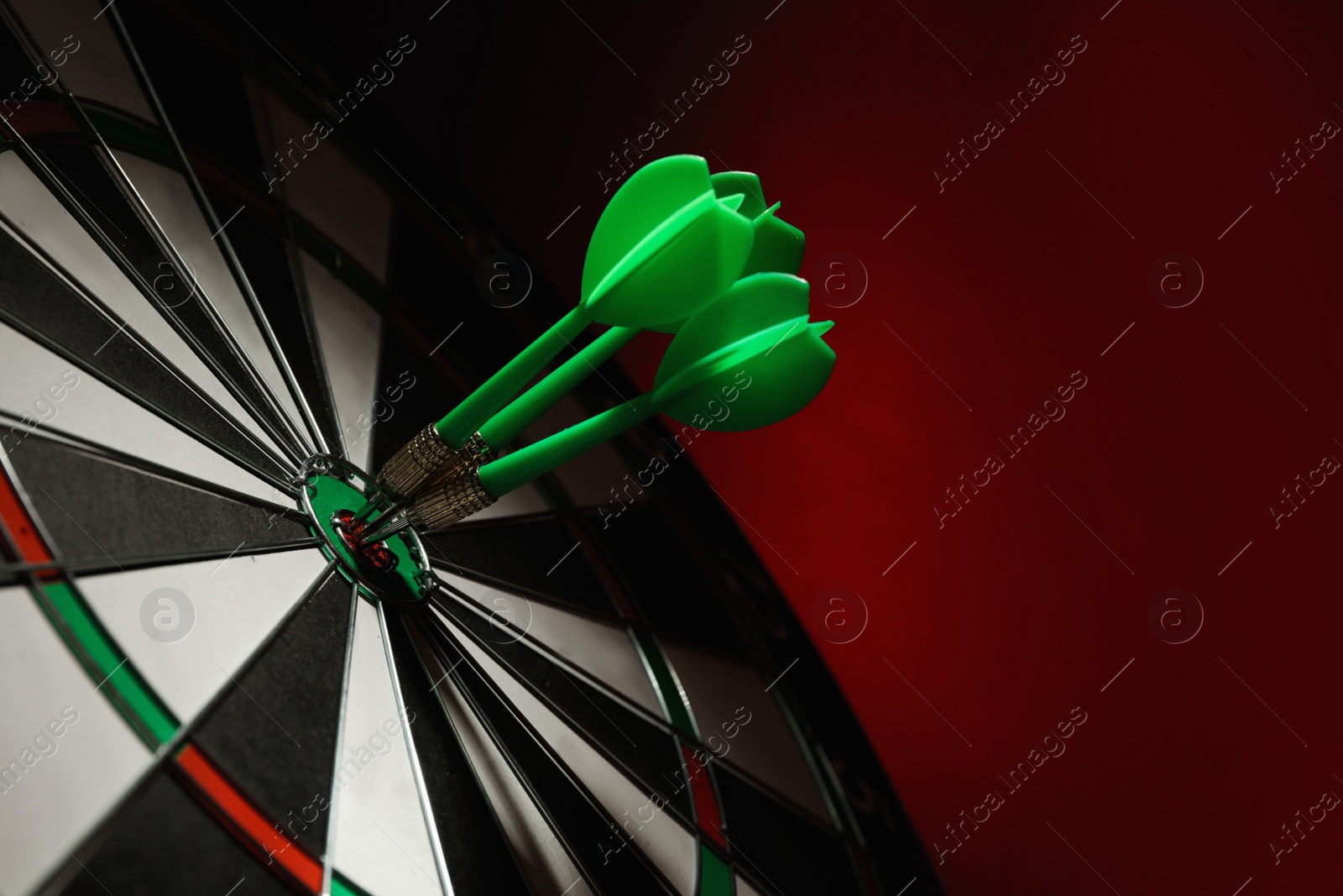 Photo of Green arrows hitting target on dart board against red background. Space for text