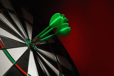 Photo of Green arrows hitting target on dart board against red background. Space for text