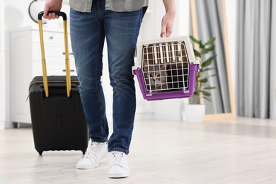 Photo of Travel with pet. Man holding carrier with cute cat and suitcase at home