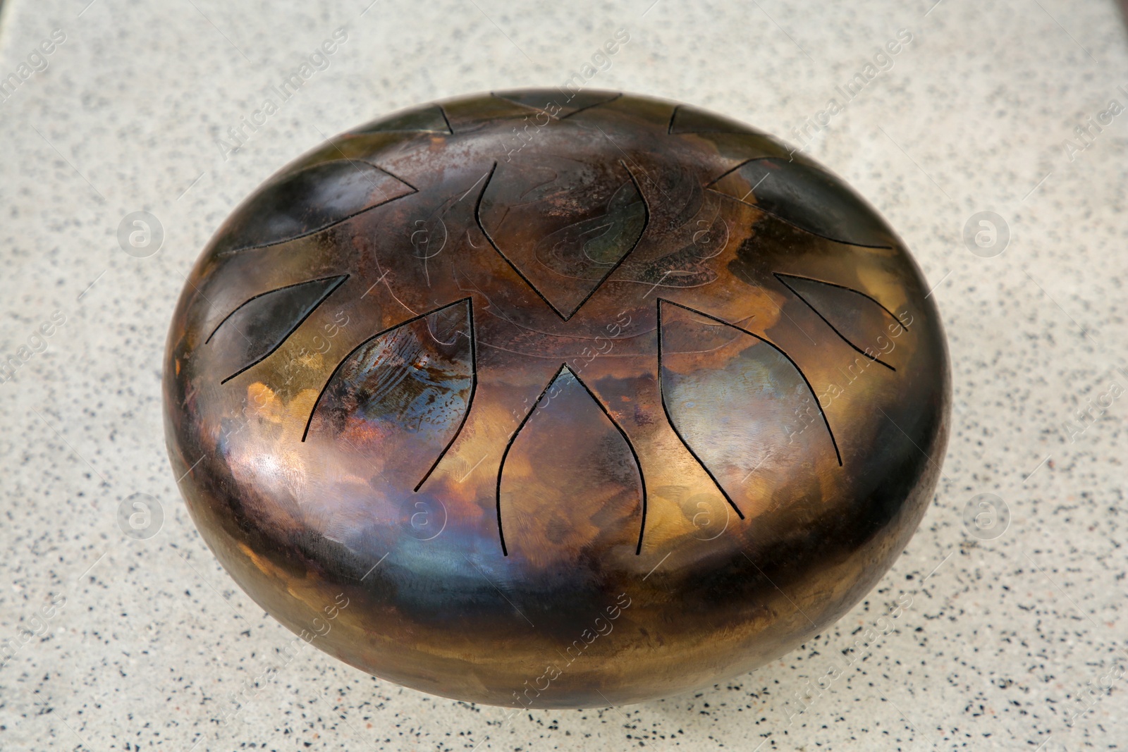 Photo of Steel tongue drum on grey table, closeup. Percussion musical instrument