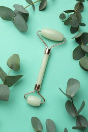 Photo of Natural face roller and eucalyptus on turquoise background, flat lay