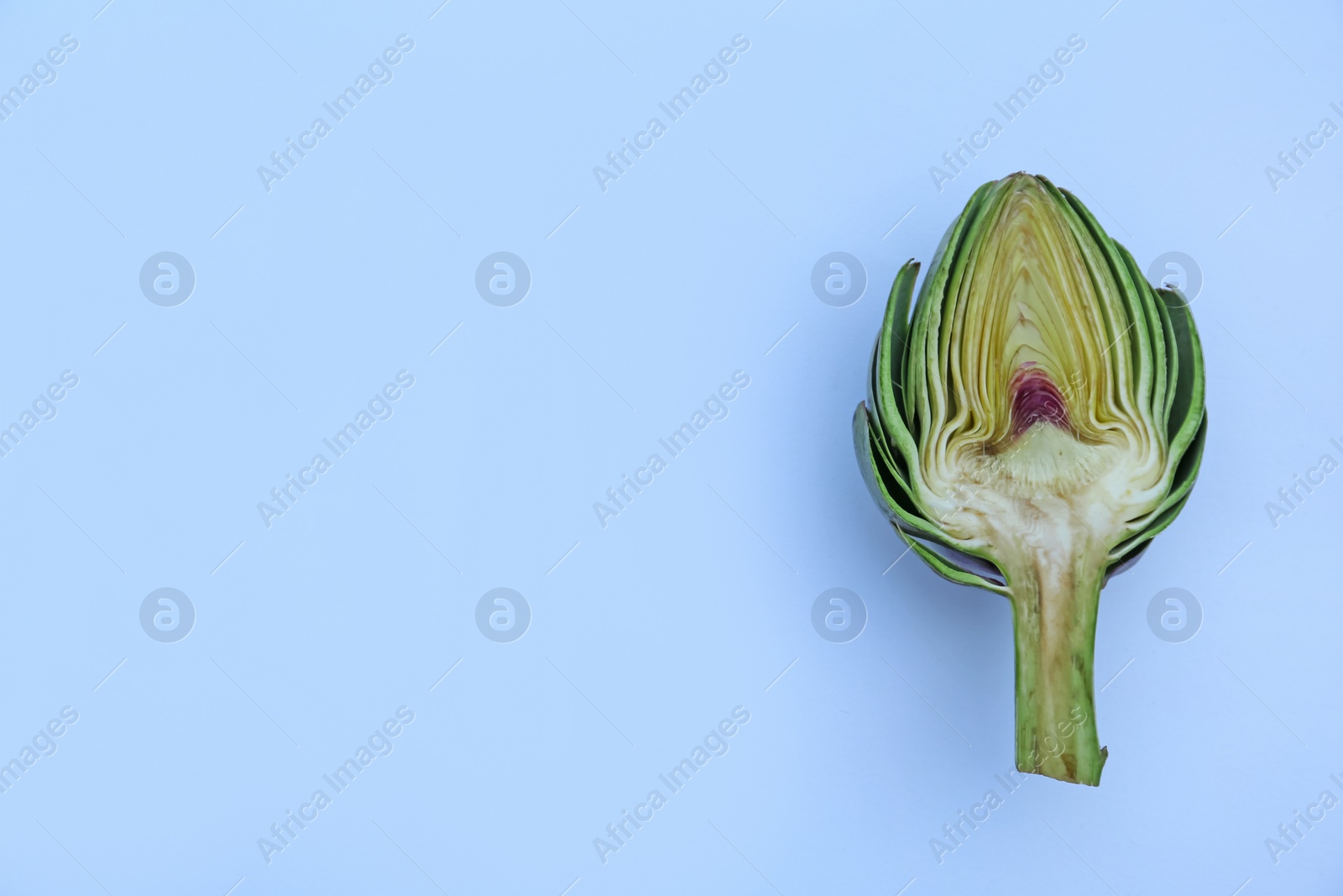 Photo of Cut fresh raw artichoke on light blue background, top view. Space for text